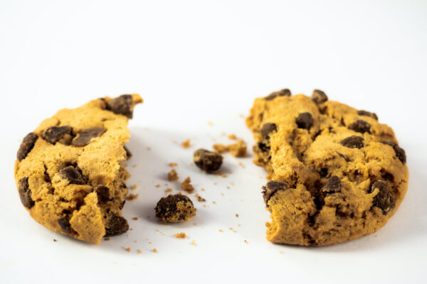 A homemade chocolate cookie with a bite and crumbs on a white background
