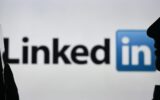 An image of a woman holding a cell phone in front of a LinkedIn logo displayed on a computer screen.