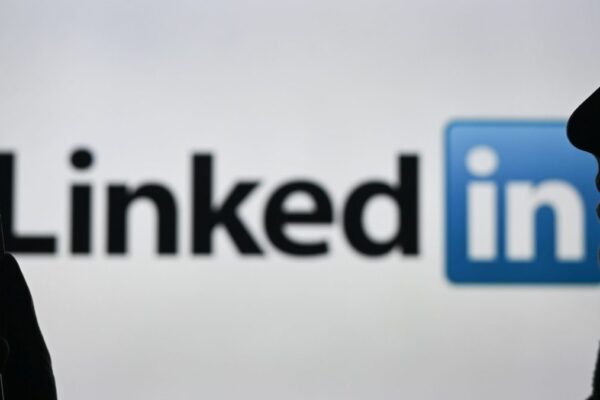 An image of a woman holding a cell phone in front of a LinkedIn logo displayed on a computer screen.