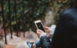 A woman using her phone while sitting on a step, to illustrate crossposting on social media