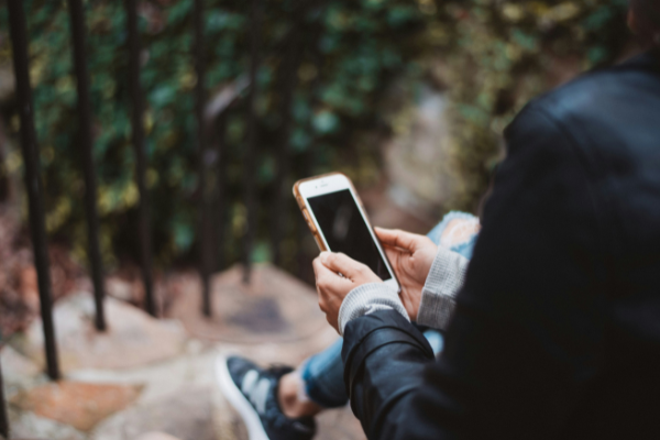 A woman using her phone while sitting on a step, to illustrate crossposting on social media