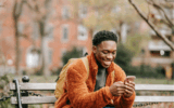 Man sits on a park bench smiling at his phone to illustrate sharing an Instagram post to Instagram Stories.