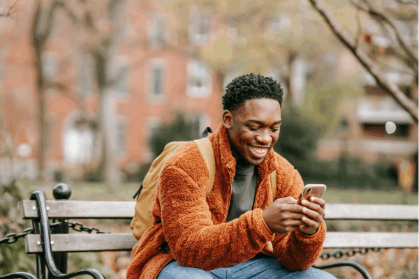 Man sits on a park bench smiling at his phone to illustrate sharing an Instagram post to Instagram Stories.