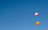 A pink and orange balloon set against the backdrop of a clear blue sky to illustrate get verified on Bluesky