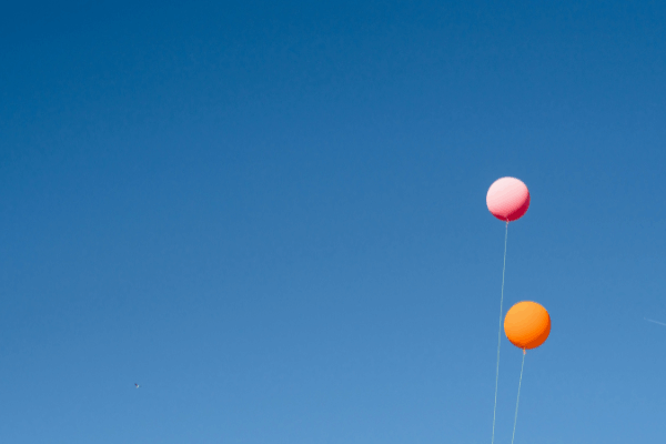 A pink and orange balloon set against the backdrop of a clear blue sky to illustrate get verified on Bluesky